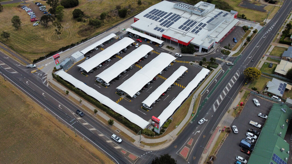 Wide aerial view of the Coles Glenvale shopping centre showing rows of white curved tensile shade canopies covering car park bays, with the Coles supermarket with rooftop solar panels and surrounding suburban roads