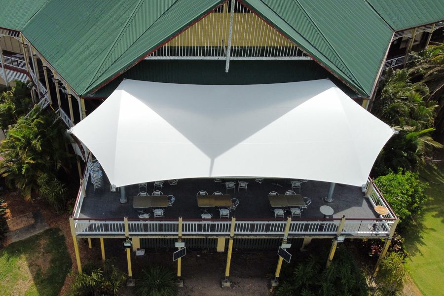 Aerial view of Colonial Golf Club showing the large white tensile shade sail from above, covering an outdoor restaurant seating area with multiple dining tables and chairs, surrounded by the colonial-style building with green roof and tropical gardens